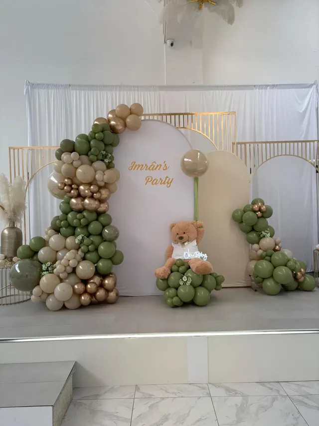 Décoration d'anniversaire avec arches, ballons verts et dorés et ourson en peluche