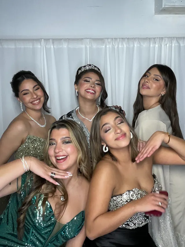 La mariée et ses amies en robes de soirée posent en riant au photobooth