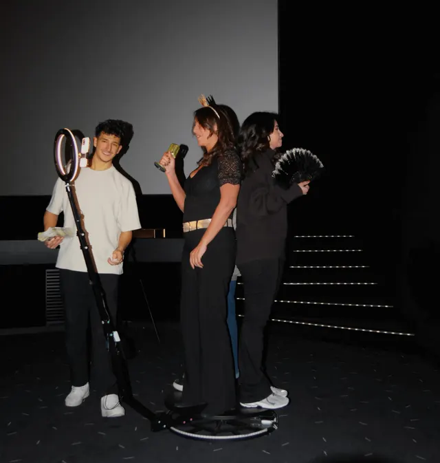 Des invités prennent la pose avec un micro doré et un éventail sur la plateforme du videobooth 360°, à côté du bras de la caméra et de son anneau lumineux